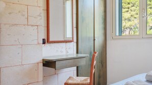 A bedroom with a bed, a wooden chair, a small table, a mirror, and a window with a view of trees. - Tiny Home 'Atenaion Otranto' with Outdoor Space (Otranto)
