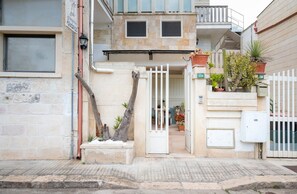 Ein Gebäude mit geschlossenem Eingangsbereich, Blumentöpfen und einem sichtbaren Balkon.