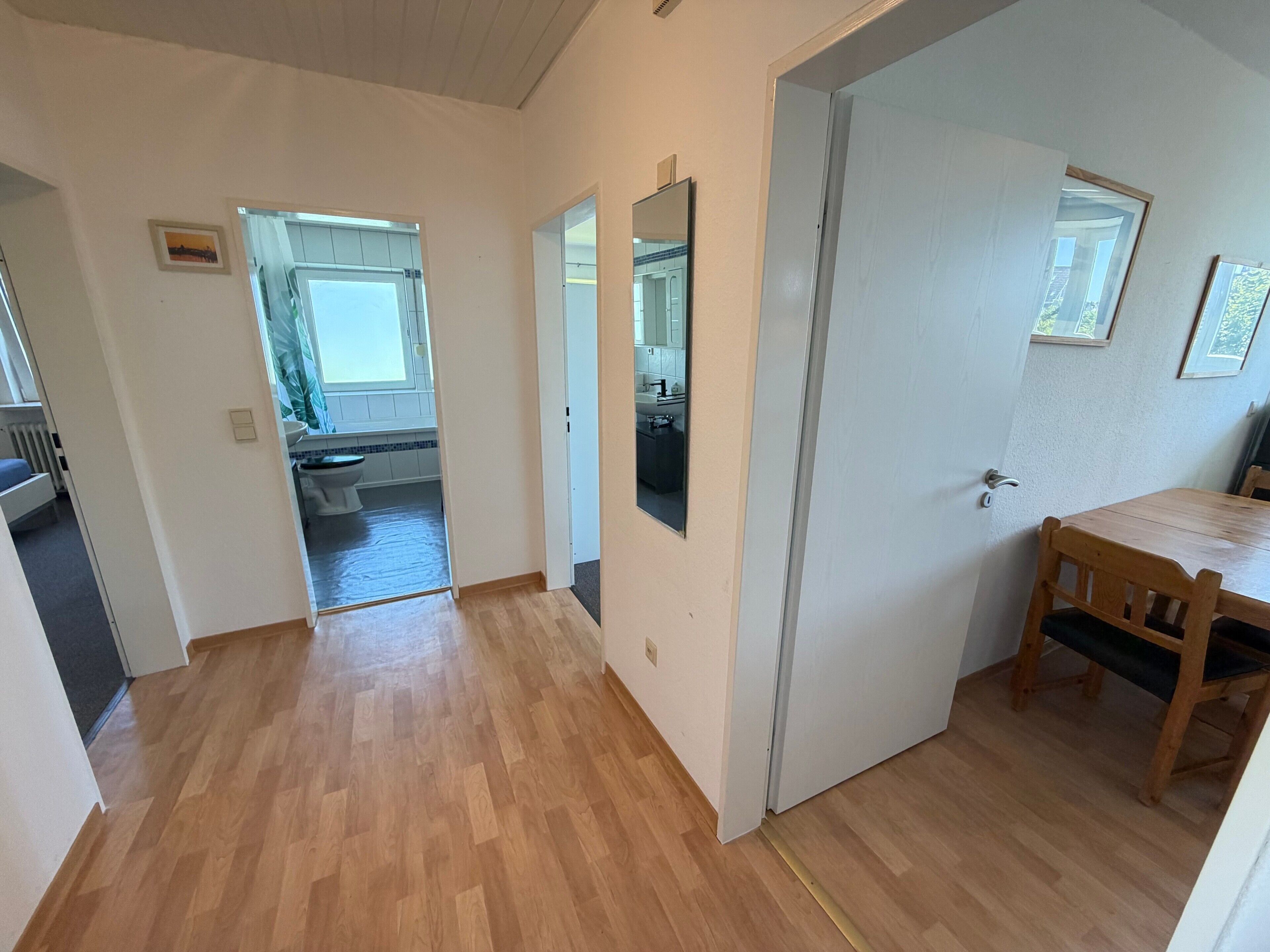 A hallway leading to a kitchen with a dining table and chairs, a door, and a window.