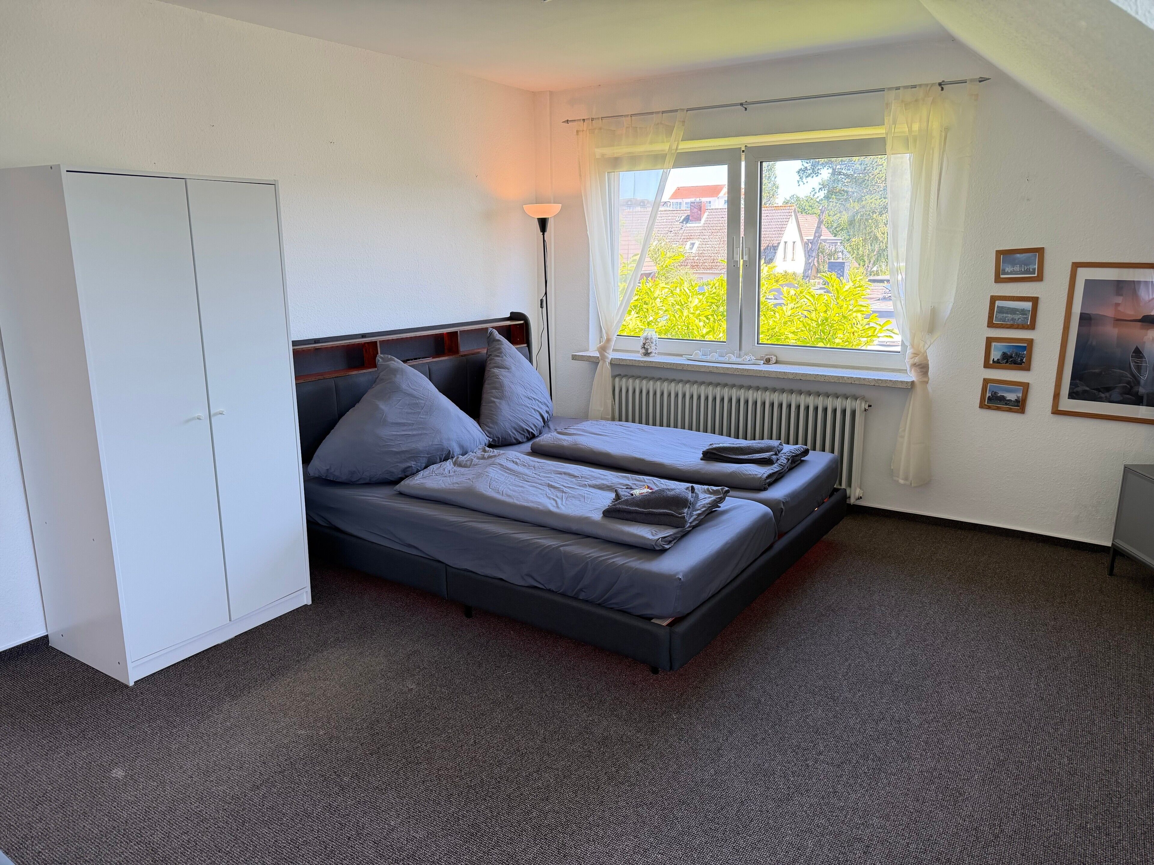 Een slaapkamer met twee bedden, een radiator, een raam met gordijnen en een kledingkast.