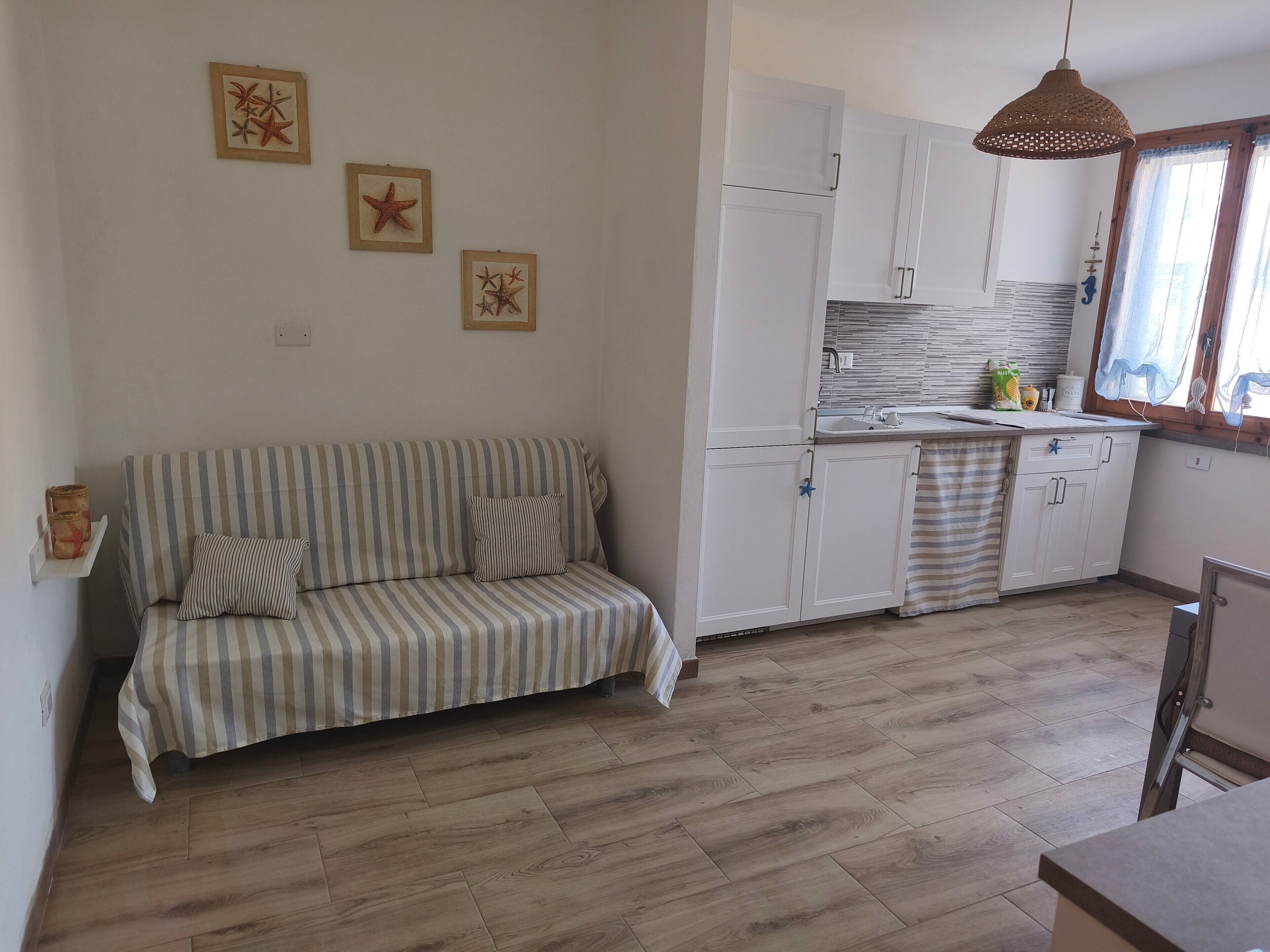 Una habitación con un sofá a rayas, una cocina con armarios blancos y una lámpara colgante.
