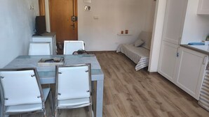 Ein Essbereich mit einem Glastisch, weißen Stühlen, einer Couch und Holzboden.