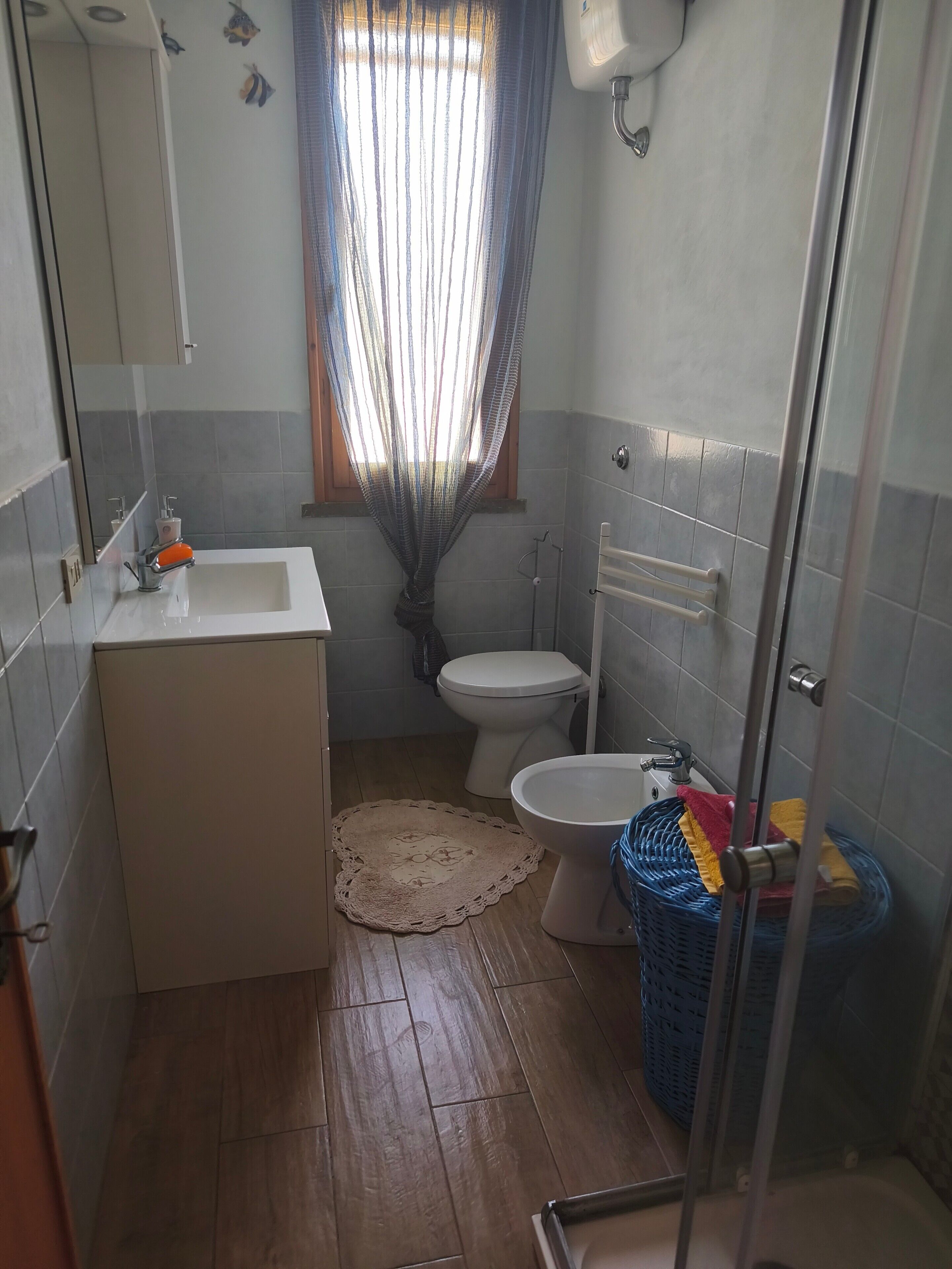 A bathroom with a sink, toilet, shower, and a window with a curtain.