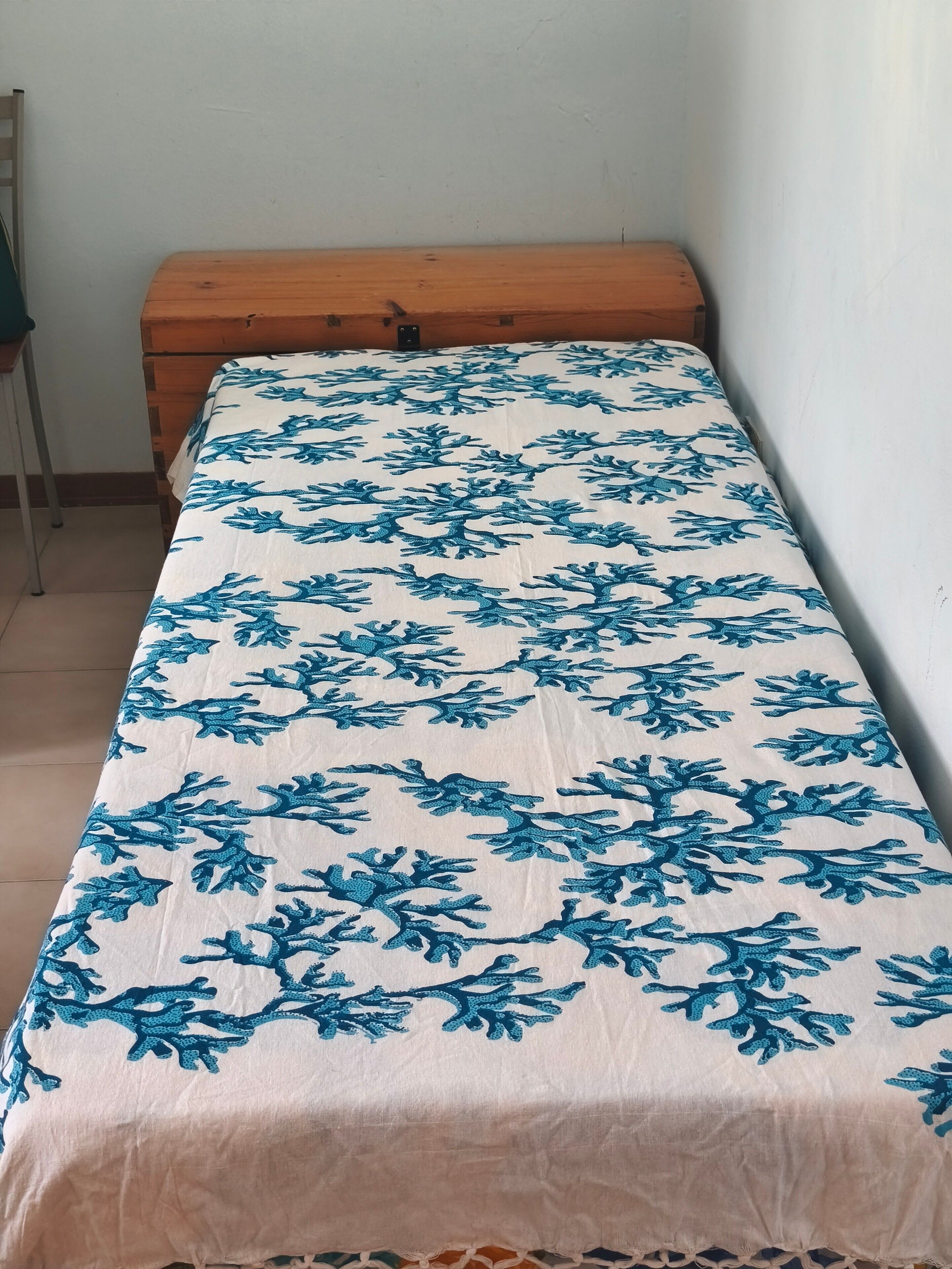 Un lit simple avec une couvre-lit à motifs, une tête de lit en bois et un mur uni.