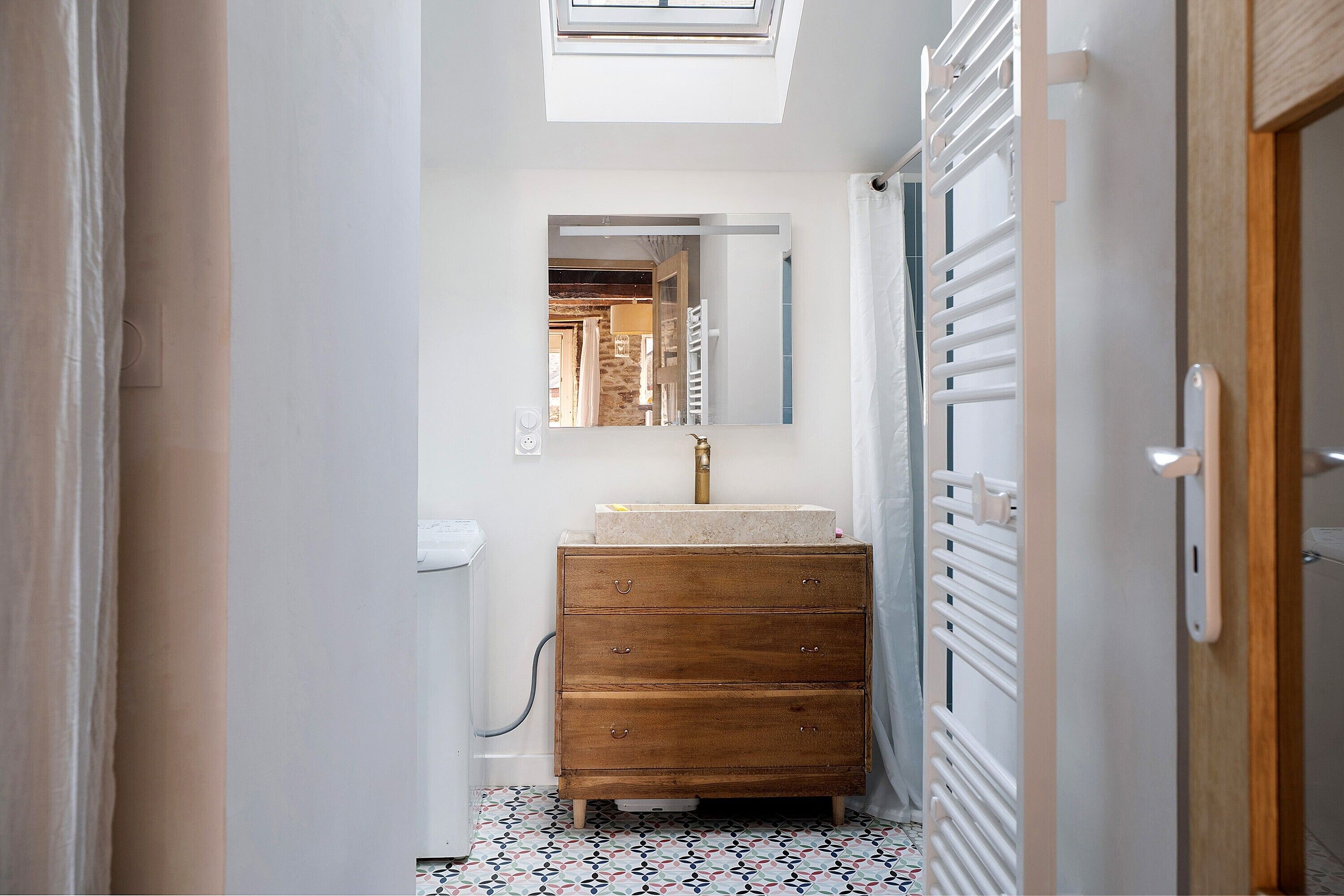 Un couloir étroit avec une commode en bois, un miroir et un radiateur.