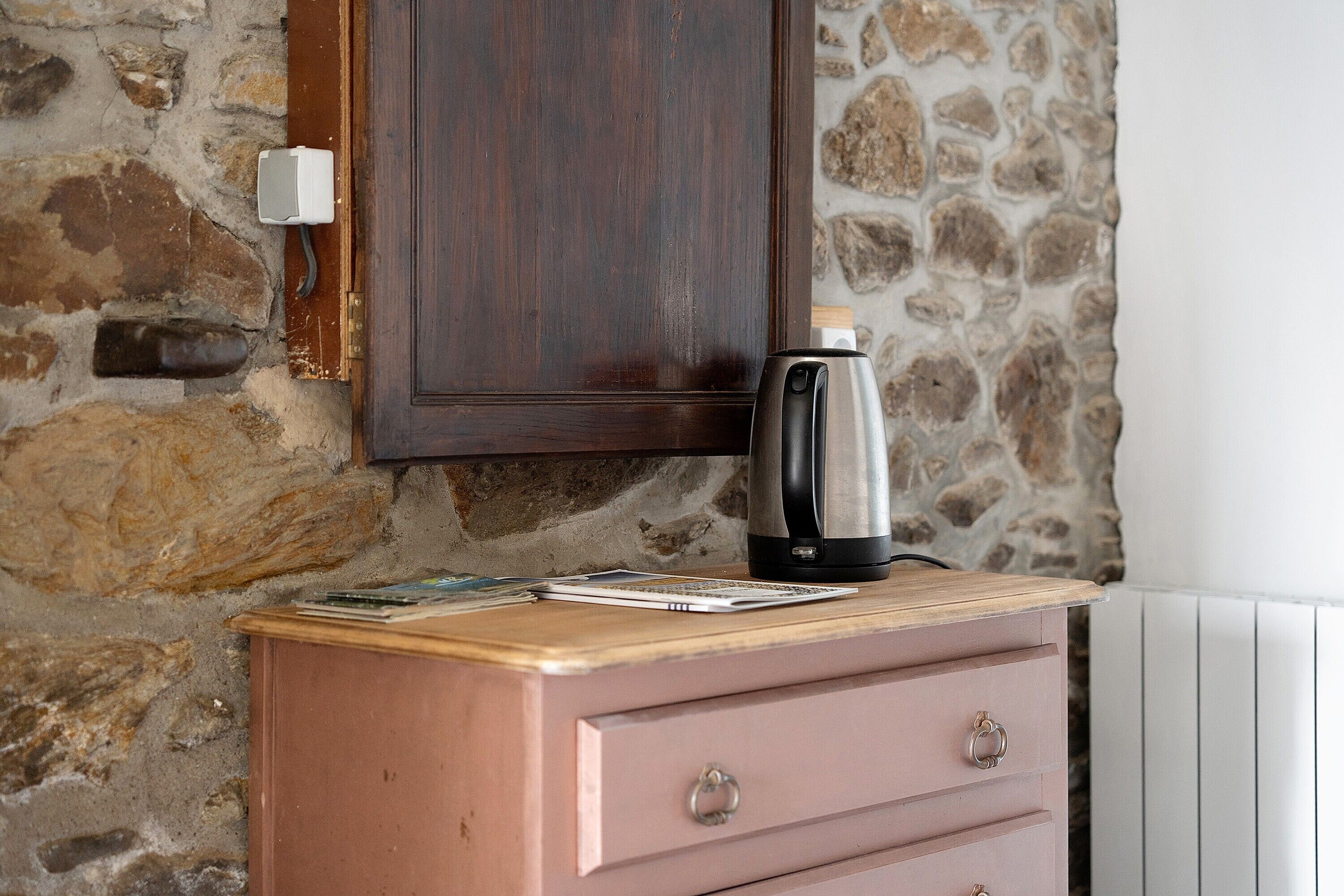 Une commode en bois sur laquelle est posée une bouilloire, un mur en pierre et une armoire en bois au-dessus.