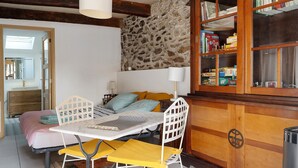 A room with a bed, a table with chairs, a bookshelf, and a stone wall.
