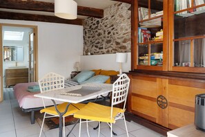 A room with a bed, a table with chairs, a bookshelf, and a stone wall.