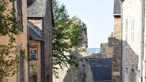 A narrow cobblestone street flanked by historic stone buildings with arched doorways and a church with a bell tower. - Au Bon Séjour (Sainte-Suzanne-and-Chammes)