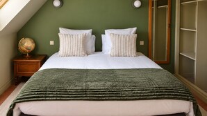 A bedroom with a bed, two pillows, a green blanket, a wooden nightstand, a globe, and a wardrobe.