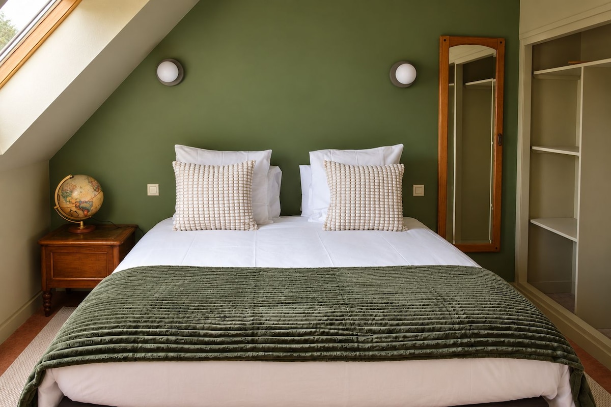 A bedroom with a bed, two pillows, a green blanket, a wooden nightstand, a globe, and a wardrobe.