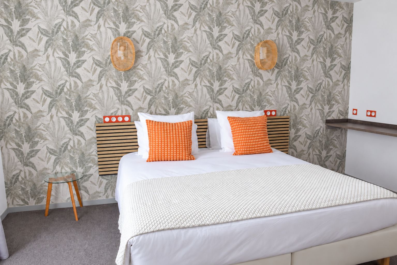 Une chambre d’hôtel avec un lit, une petite table et un mur orné d’un motif de feuilles.