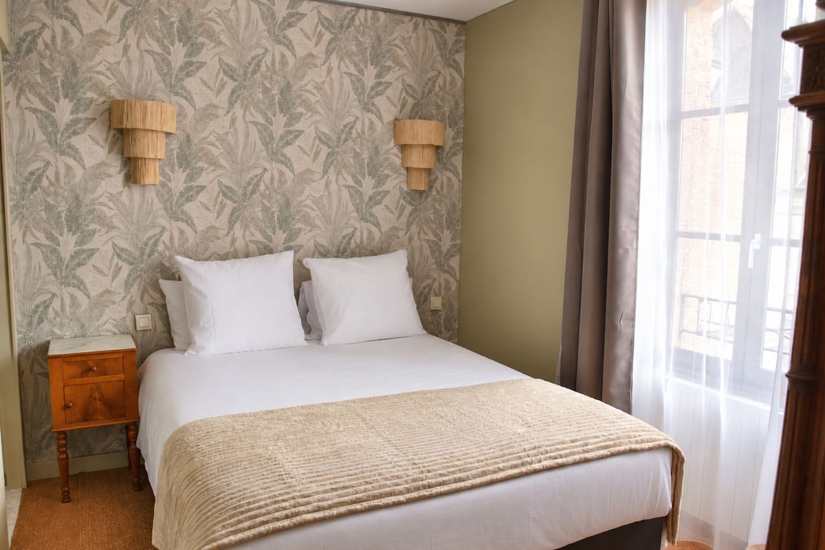 A hotel room with a bed, two bedside lamps, a nightstand, and a window with curtains.
