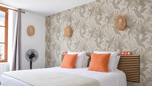 A bedroom with a bed, two pillows, a bedside fan, and a window with curtains.