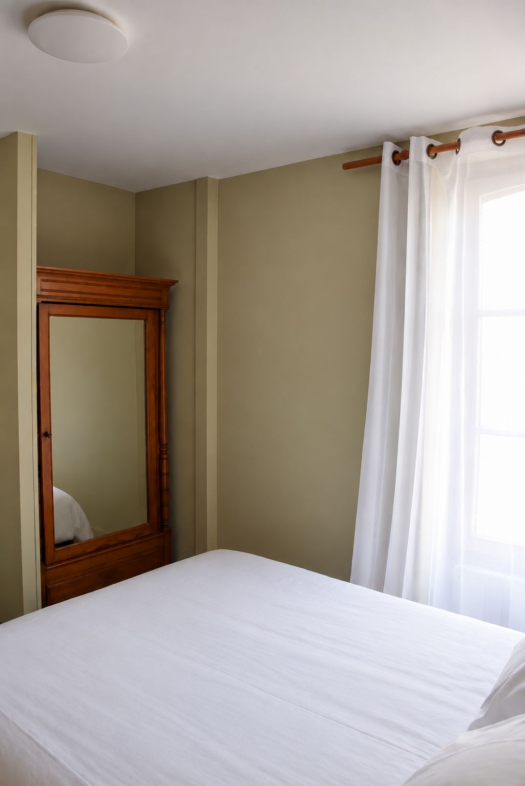 A bedroom with a bed, a wooden wardrobe, and a window with curtains.