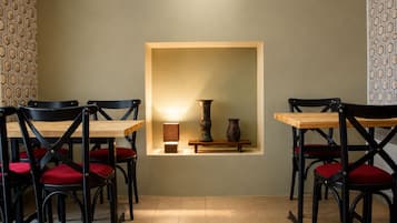 Un comedor con una mesa y sillas, un estante de pared con adornos, y papel tapiz estampado.