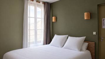 A hotel room with a large bed, a window with curtains, and a wall-mounted lamp.