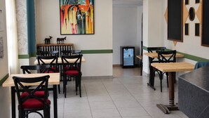 A restaurant interior with multiple tables and chairs, a painting on the wall, and a refrigerator.