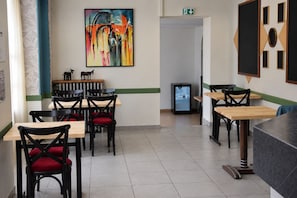 A restaurant interior with multiple tables and chairs, a painting on the wall, and a refrigerator.