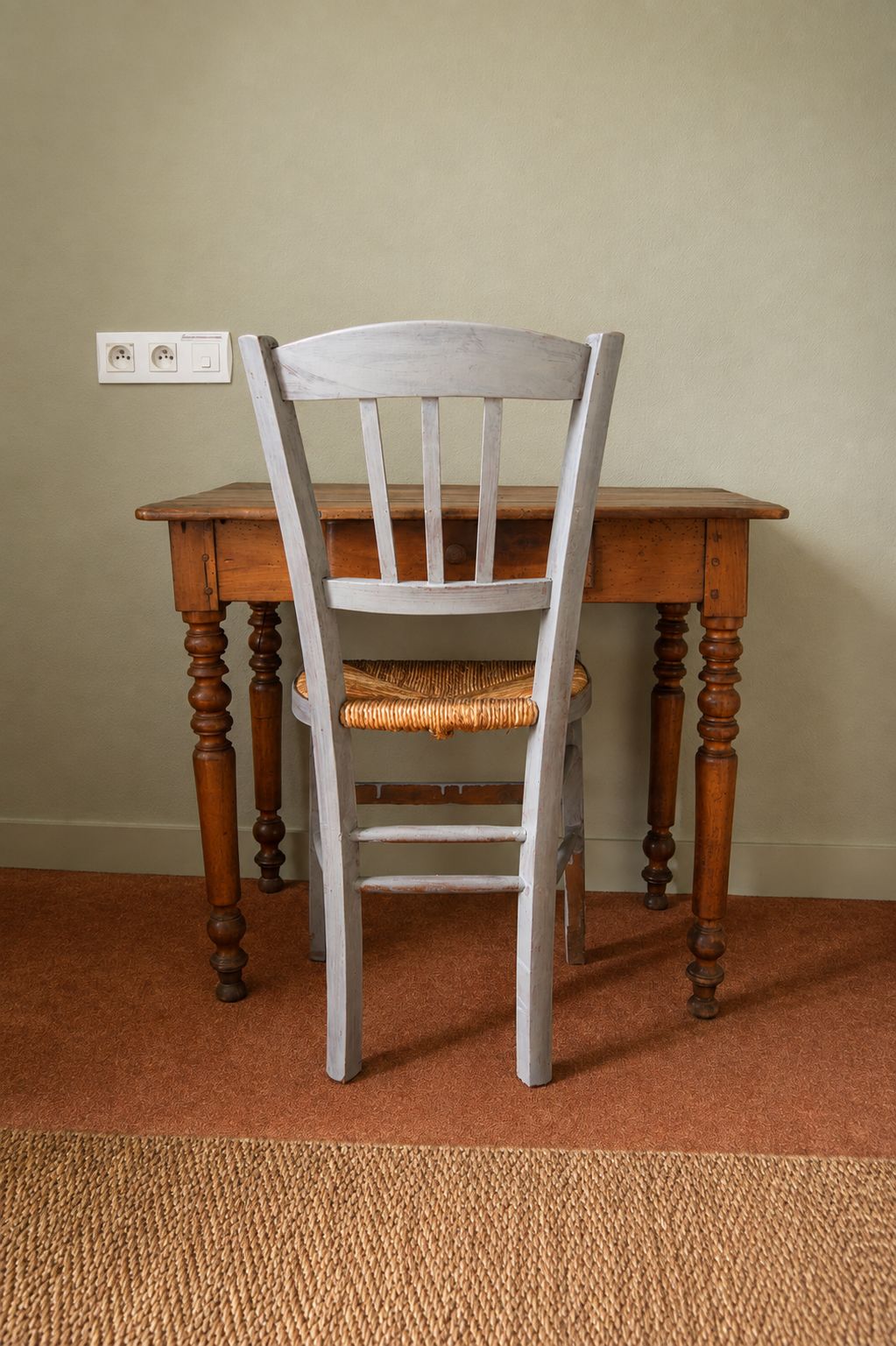 Ein Stuhl mit gewobener Sitzfläche und Lehne, vor einem Holztisch mit gedrehten Beinen platziert.