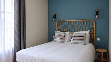 Una cama con colchón blanco y almohadas a rayas, cabecera de madera y dos lámparas fijadas a la pared.