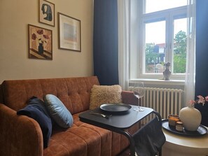 Ein Wohnzimmer mit braunem Sofa, einem kleinen Tisch, einer Blumenvase und gerahmten Bildern an der Wand.