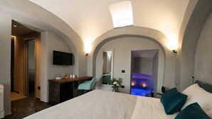 Habitación de hotel con cama, escritorio, televisor y zona de estar con vista a una piscina.