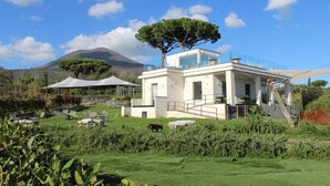 Una casa moderna con un invernadero de vidrio, mobiliario exterior y una montaña al fondo.