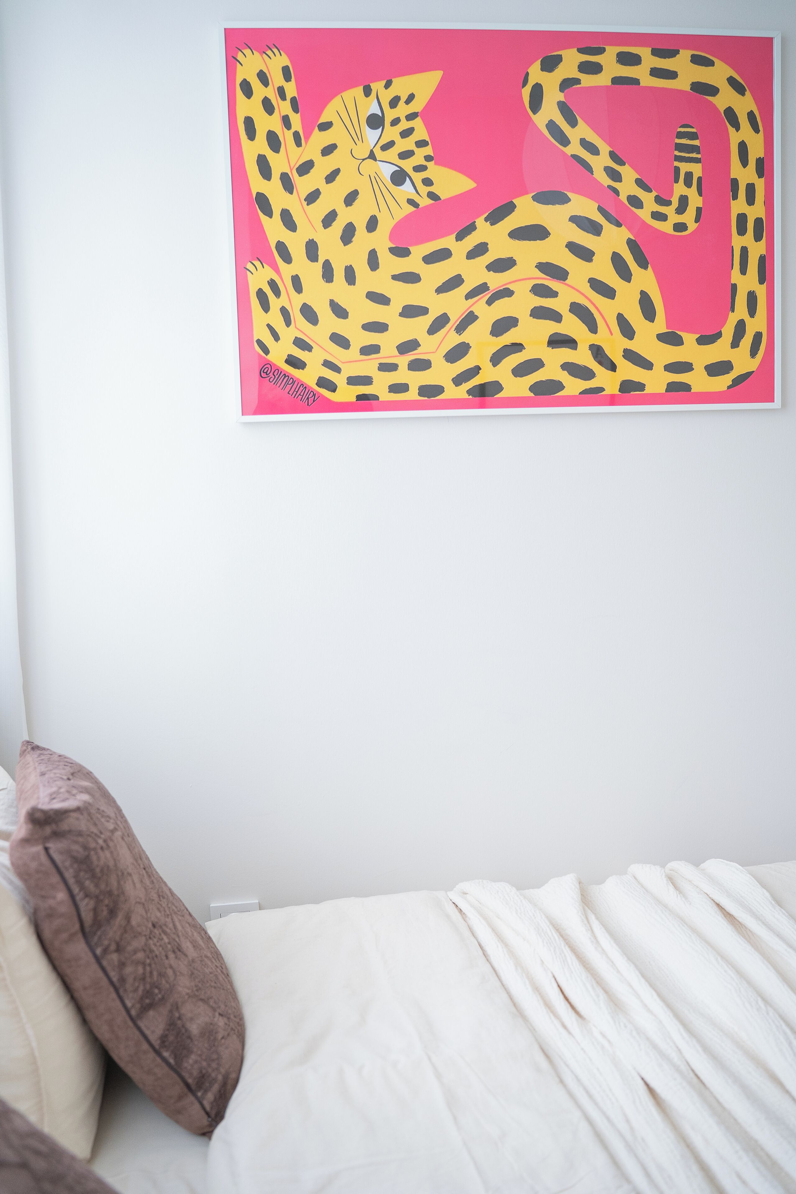Une chambre à coucher avec un lit, un oreiller et un tableau représentant un léopard, accroché au mur.