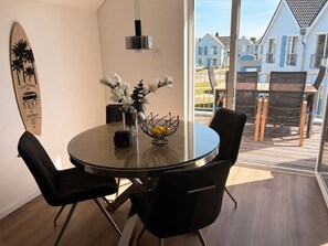 A round dining table with black chairs, a vase with white flowers, and a surfboard decoration on the wall. - Klabauter-Kajüte - Balcony, private parking space, washing machine, infrared cab (Olpenitz)