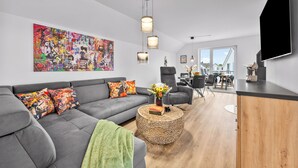 Una sala moderna con un sofá gris, obras de arte coloridas y un comedor con vistas.