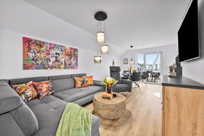 A modern living room with a grey sofa, colorful artwork, and a dining area with a view. - Klabauter-Kajüte - Balcony, private parking space, washing machine, infrared cab (Olpenitz)
