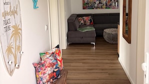 Un pasillo con un banco de madera, un sofá gris, una obra de arte de colores y un ventilador de techo.