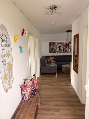 A hallway with a wooden bench, a gray sofa, a colorful wall art piece, and a ceiling fan. - Klabauter-Kajüte - Balcony, private parking space, washing machine, infrared cab (Olpenitz)