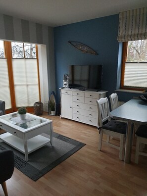 A modern living room with a television, white furniture, and a large window. - Modern seaside apartment with partial sea view and family-friendly amenities (Schönberger Strand)