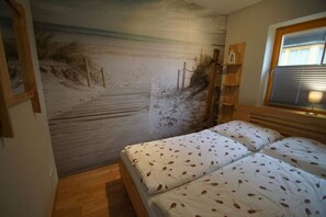 Ein Schlafzimmer mit Wandmalerei zum Strandthema, einem Doppelbett und einem Fenster mit Jalousien.