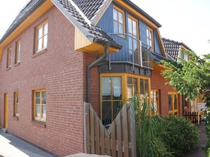 Une maison à deux étages, construite en briques, avec un balcon, une clôture en bois et un jardin.