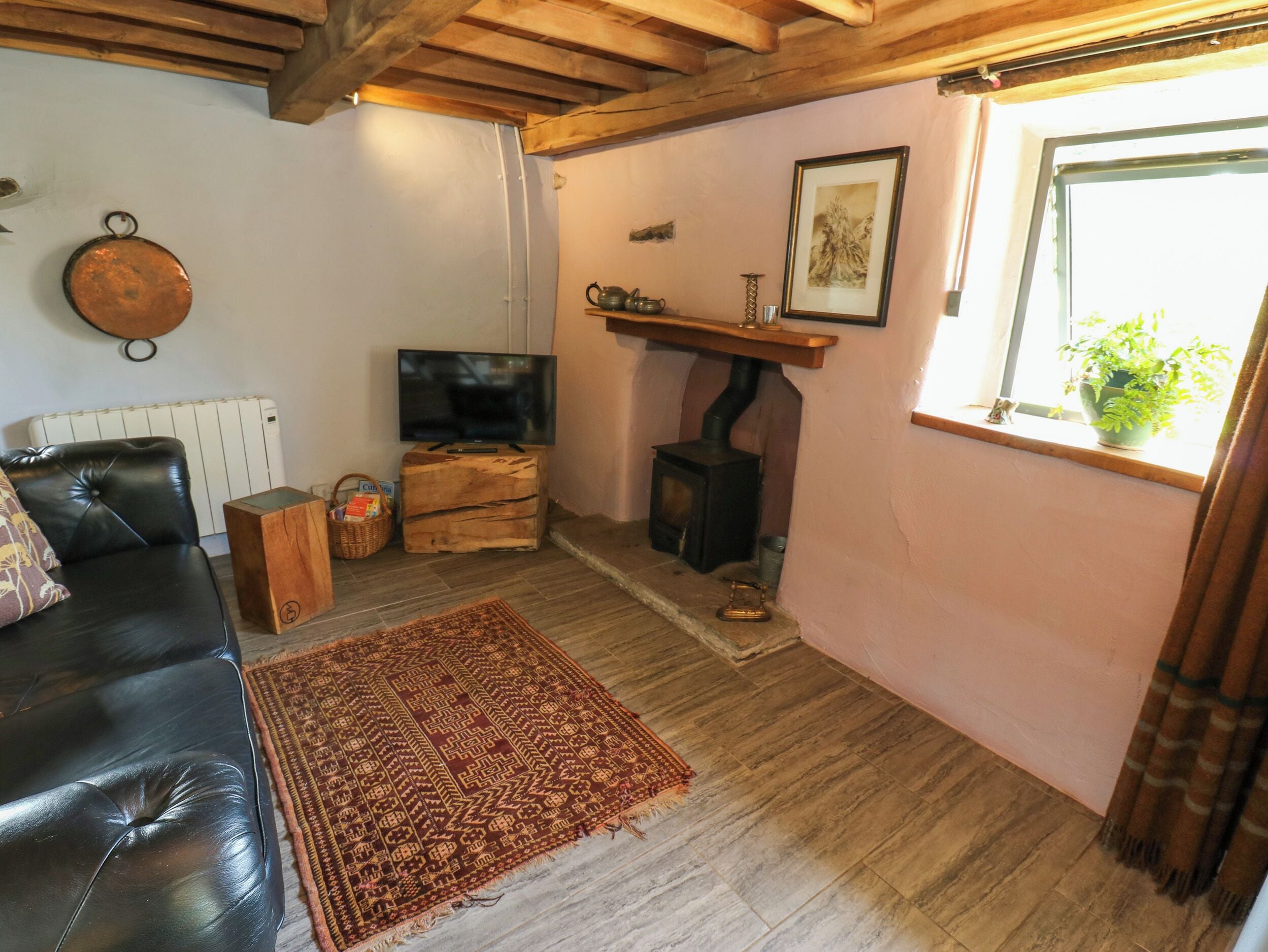 A living room with a black leather sofa, a television, a wooden cabinet, a fireplace, and a window with a plant.