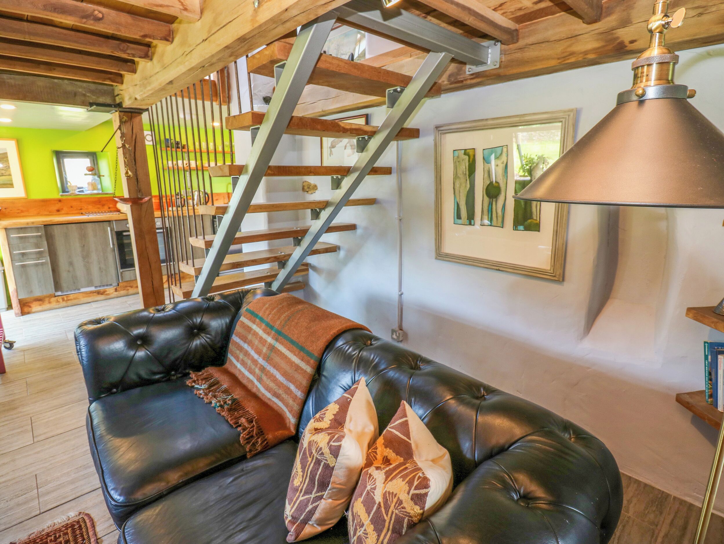 A black leather sofa with patterned cushions, a wooden staircase, and a framed artwork on the wall.