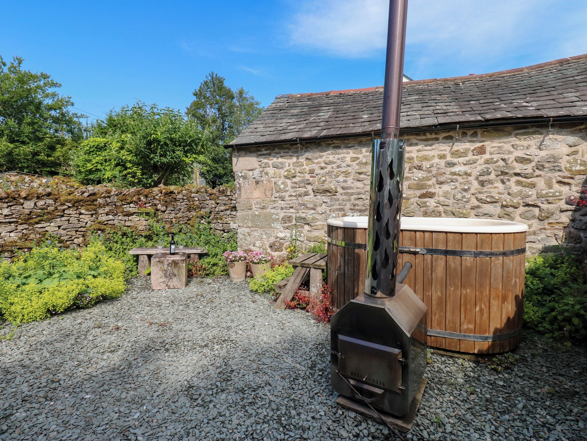 A stone building with a wooden barrel, a metal chimney, and a gravel path.