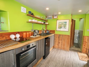 A kitchen with wooden cabinets, a built-in oven, a sink, and a green wall. - The Brew House (Penrith)