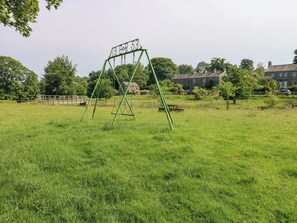 A grassy field with a swing set and a wooden bench. - The Brew House (Penrith)
