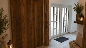 Una porta scorrevole in legno, una porta bianca con pannelli di vetro, un tappetino nero, un divano beige e un tavolino con una candela e un lampione.