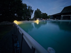 Ein Schwimmbad mit Zaun, Bäumen und einem Gebäude im Hintergrund.