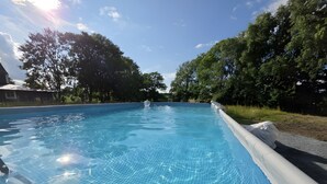 Una piscina limpida con fondo piastrellato, circondata da alberi e un edificio sullo sfondo.