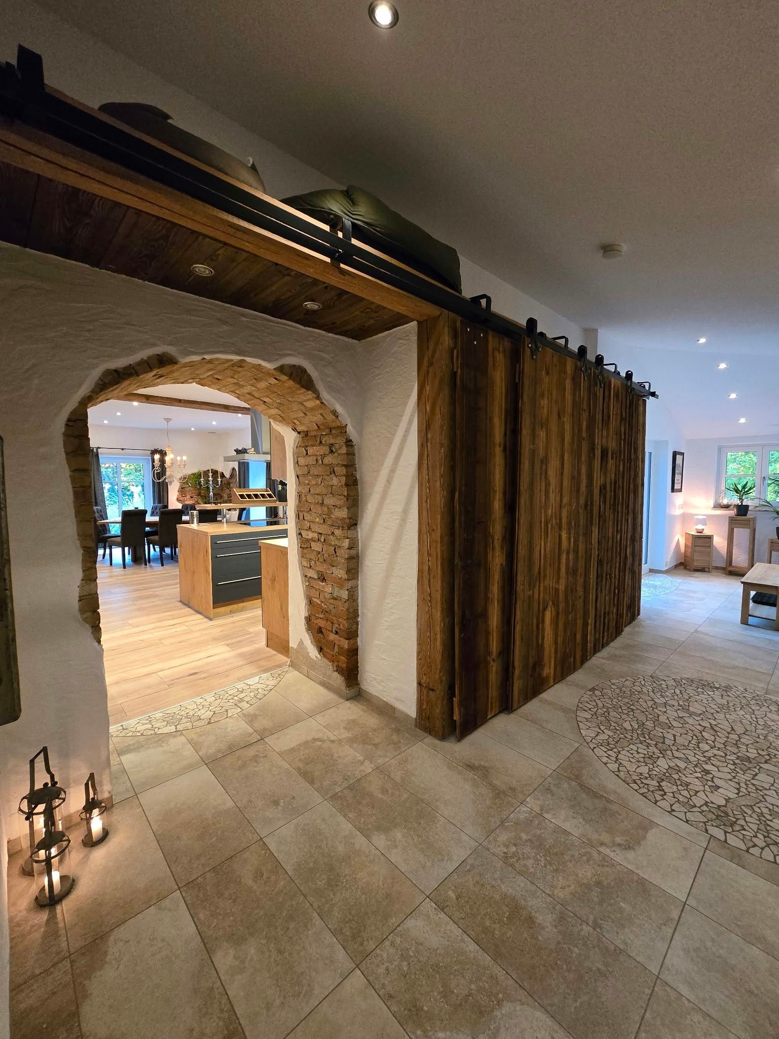 A modern interior with a stone archway leading to a kitchen and dining area, a wooden sliding door, and a tiled floor.