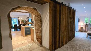 A modern interior with a stone archway leading to a kitchen and dining area, a wooden sliding door, and a tiled floor.