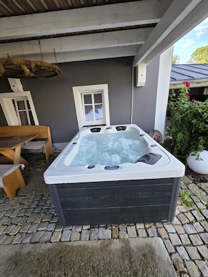 Ein Whirlpool mit Bedienelementen, eine Holzbank, ein Fenster und eine terrasse mit Steinpflaster.