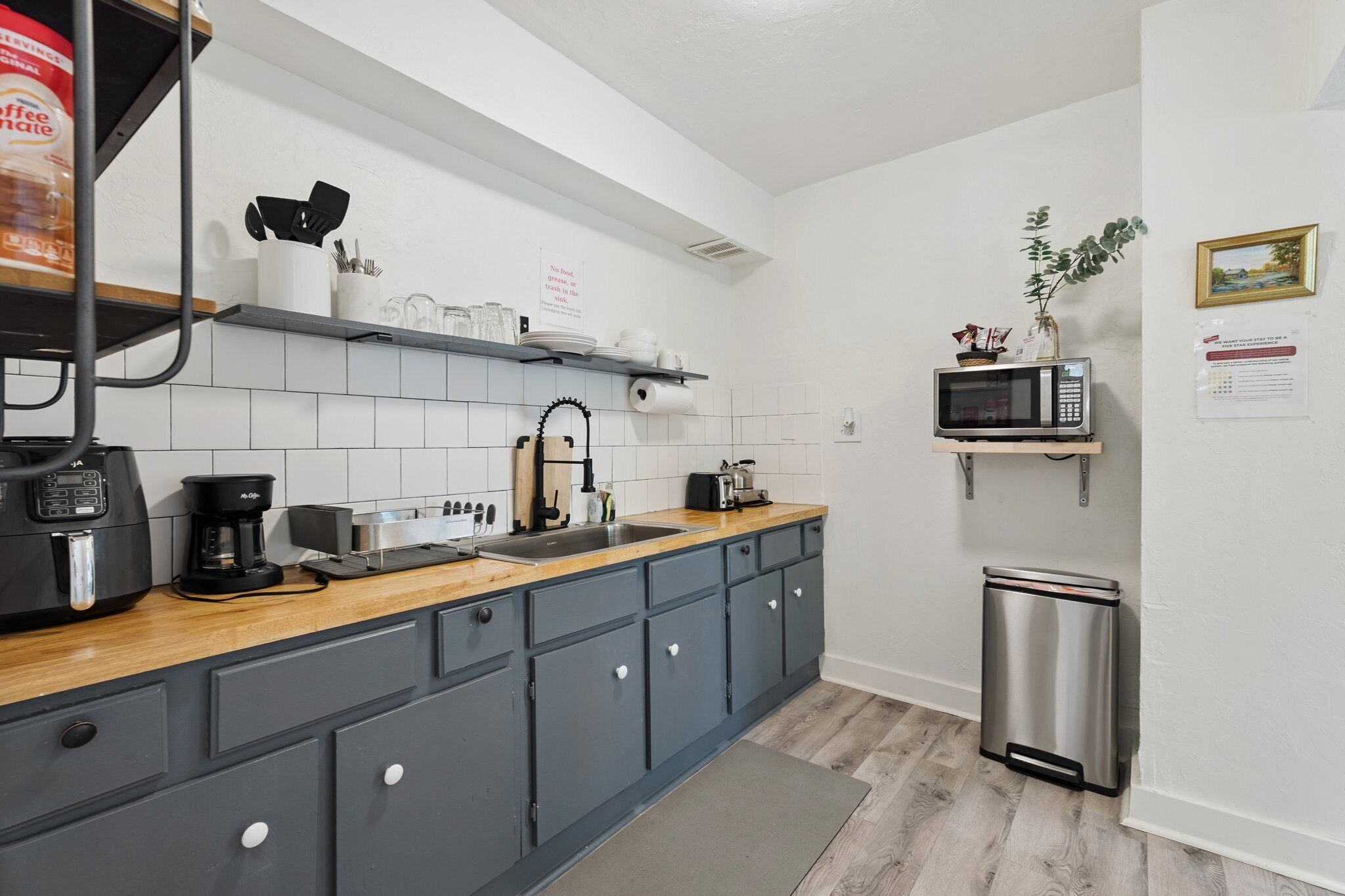 Una cocina compacta con armarios grises, encimera de madera, cafetera, microondas y un cubo de basura.