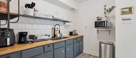 Una cocina compacta con armarios grises, encimera de madera, cafetera, microondas y un cubo de basura.